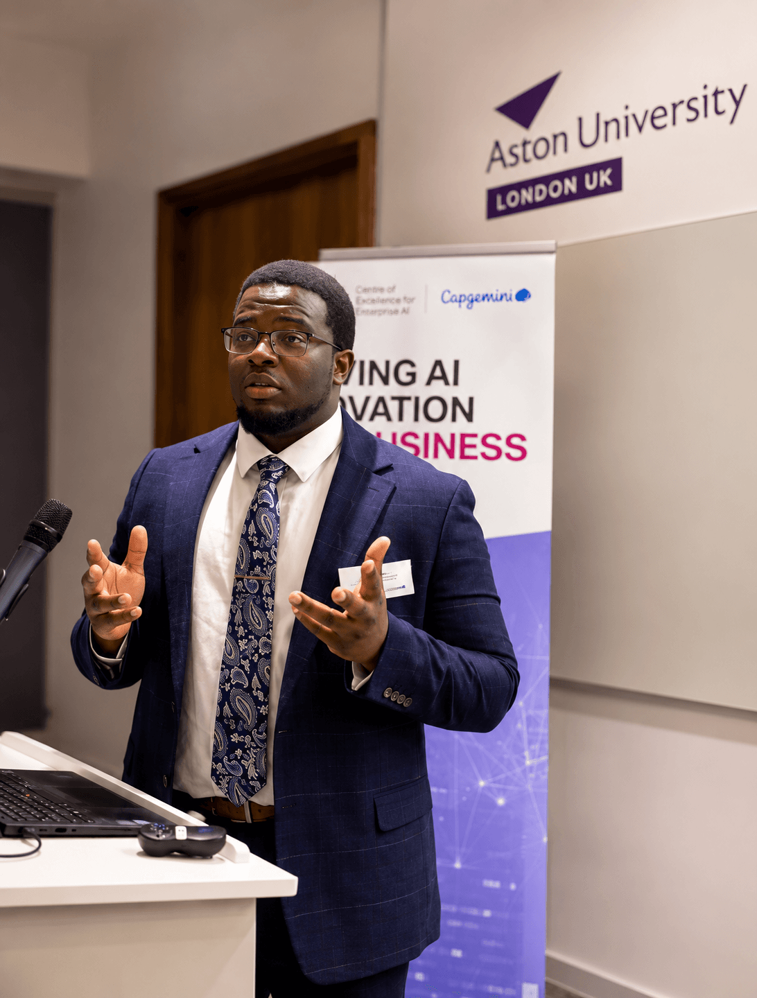 Lionel Muskwe presenting at a podium at Aston University London, in front of a Centre of Excellence for Enterprise AI and Capgemini banner